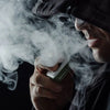Man using a vaping mod and exhaling vapor in a black studio setting, representing vaping and electronic cigarette use