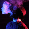 man wearing a hat blowing smoke in a dark background