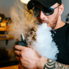 Bearded man wearing sunglasses and smoking an electronic cigarette, representing vaping and e-cigarette use