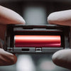 Close-up of gloved hands holding a red cylindrical object in a controlled professional setting