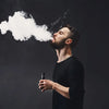 Man using a vaping mod and exhaling vapor in a black studio setting, representing vaping and electronic cigarette use
